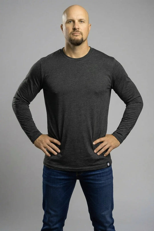 Man wearing a dark gray long-sleeve shirt and blue jeans against a gray background