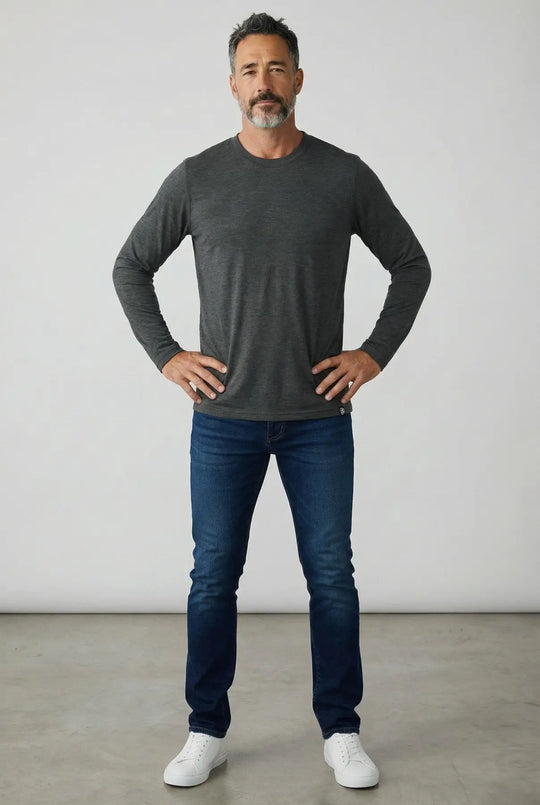 Man wearing a dark gray long-sleeve shirt and blue jeans standing against a plain background
