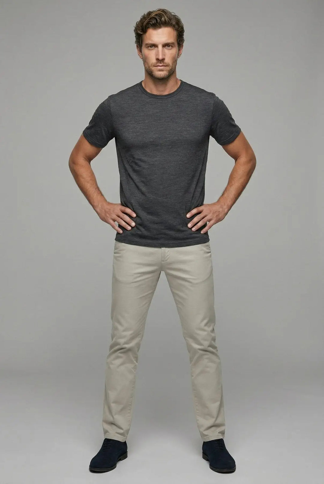 Man wearing a dark gray t-shirt and light beige pants against a plain background