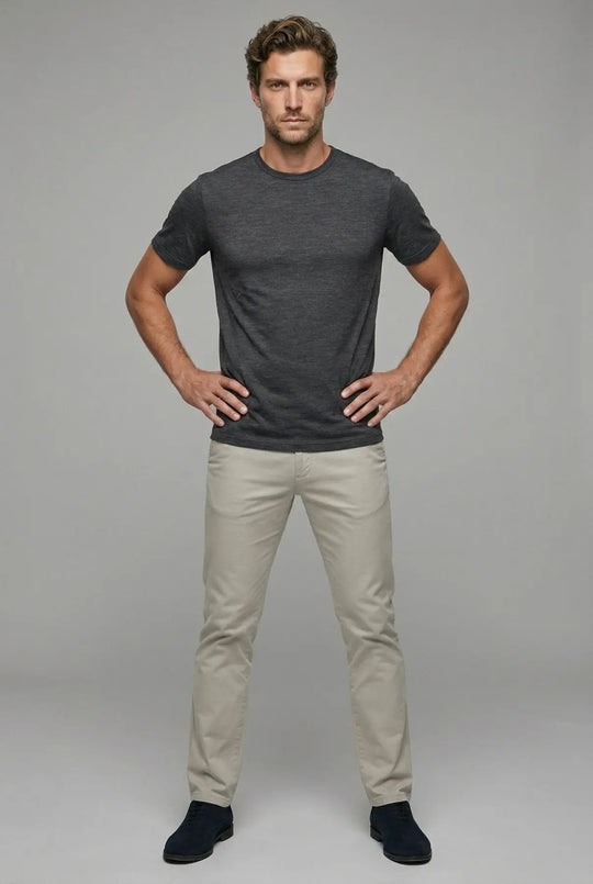 Man wearing a dark gray t-shirt and light beige pants against a plain background