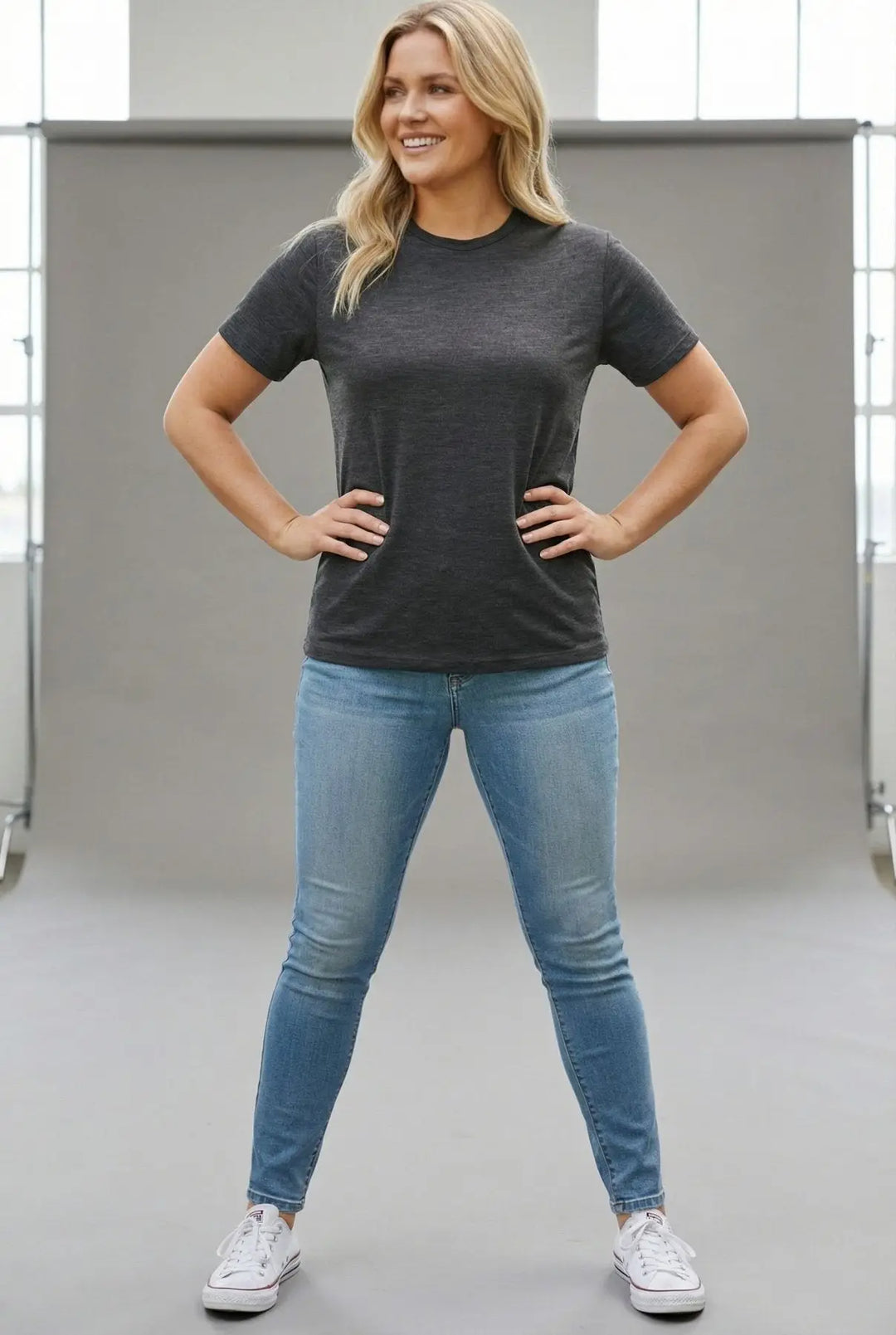 Woman wearing a dark gray t-shirt and blue jeans standing in a neutral setting
