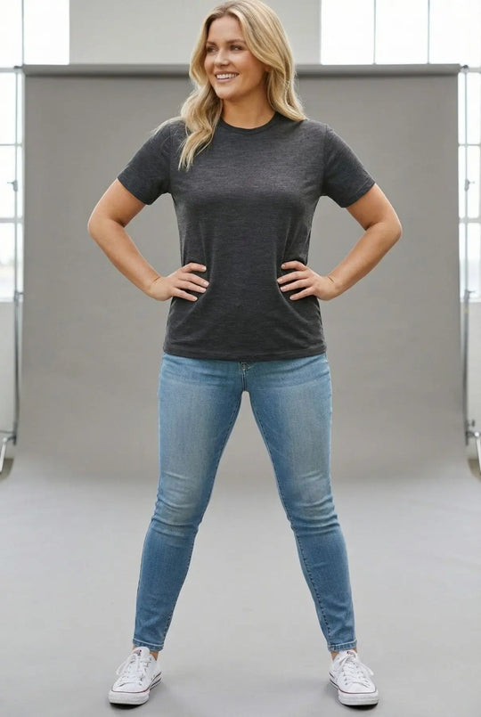 Woman wearing a dark gray t-shirt and blue jeans standing in a neutral setting