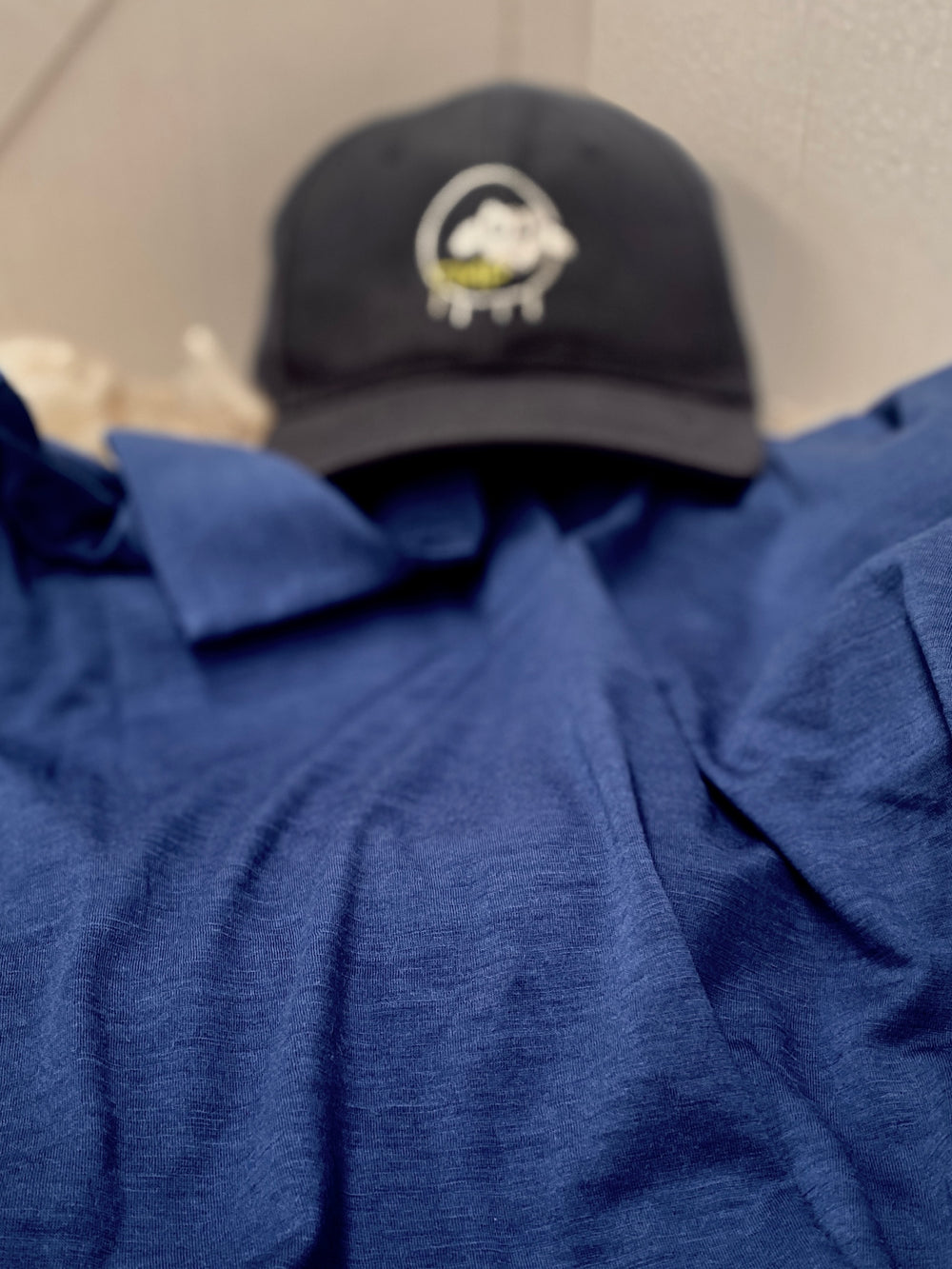 Black cap with a logo on a blue shirt against a neutral background