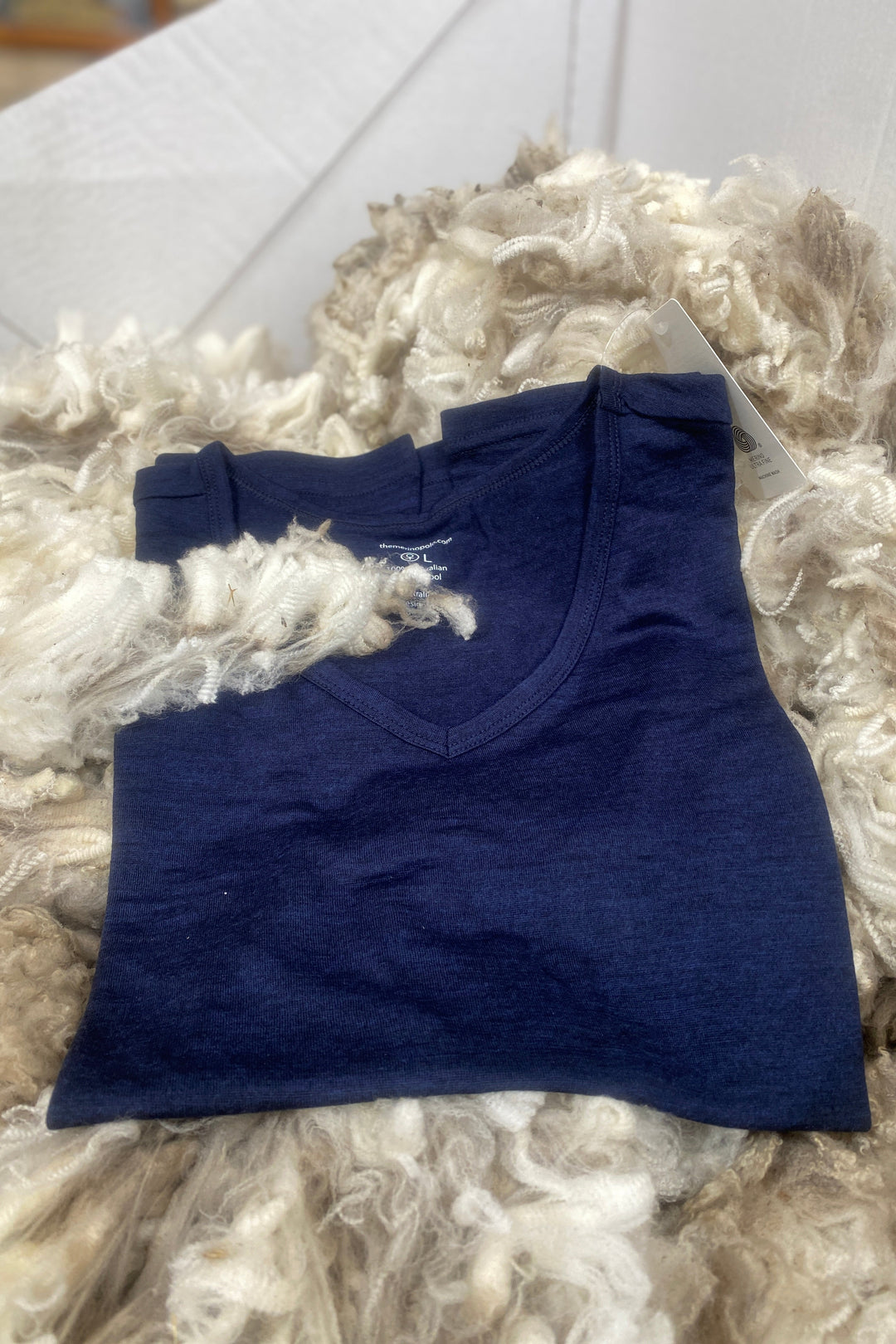 Folded merino blue t-shirt on a textured white surface