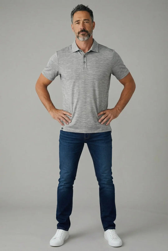 Man wearing a gray polo shirt and blue jeans standing against a gray background