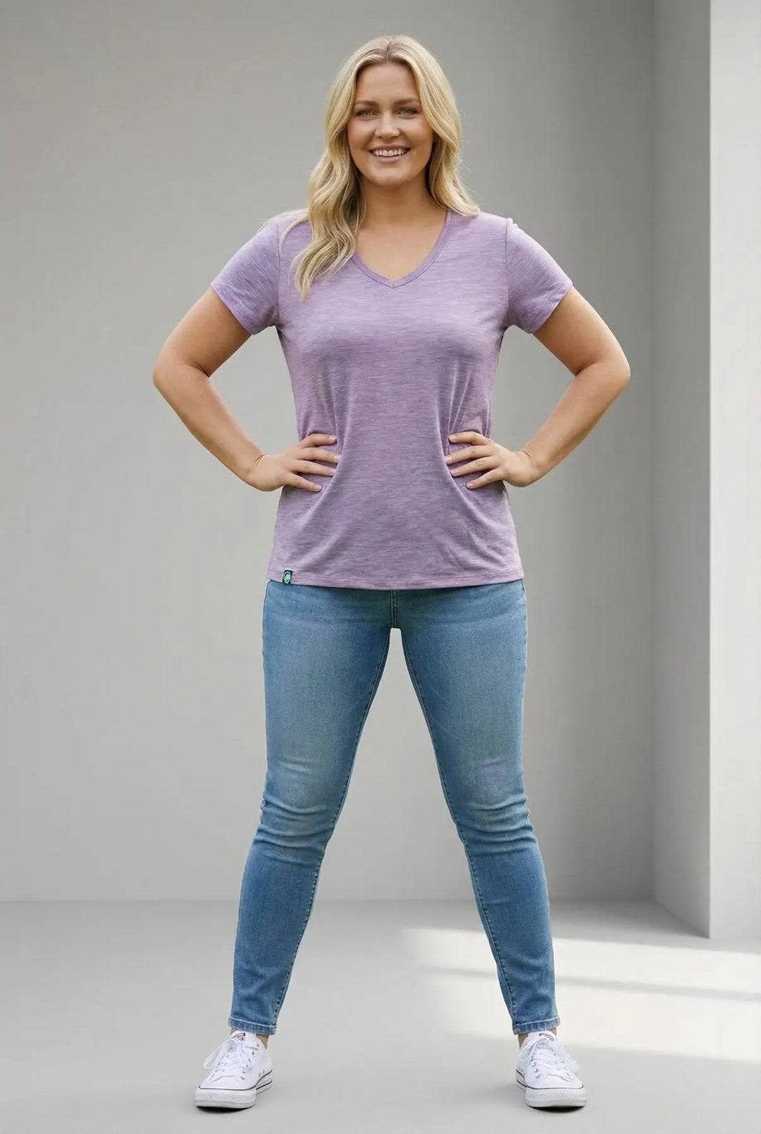 Woman wearing a purple t-shirt and blue jeans standing against a plain background