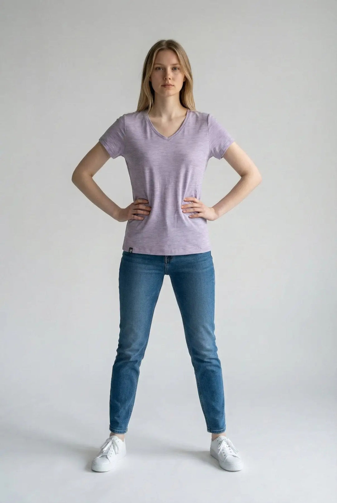 Woman wearing a light purple t-shirt and blue jeans on a plain background