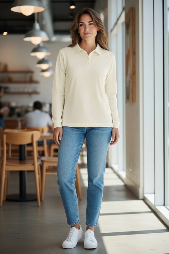 Woman wearing a cream long-sleeve shirt and blue jeans standing in a modern cafe.