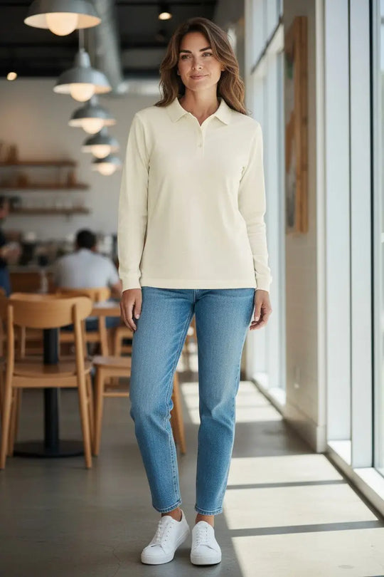 Woman wearing a cream long-sleeve shirt and blue jeans standing in a modern cafe.