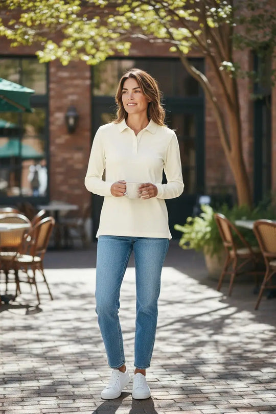 Woman in a cream white shirt and blue jeans standing outdoors on a sunny day.