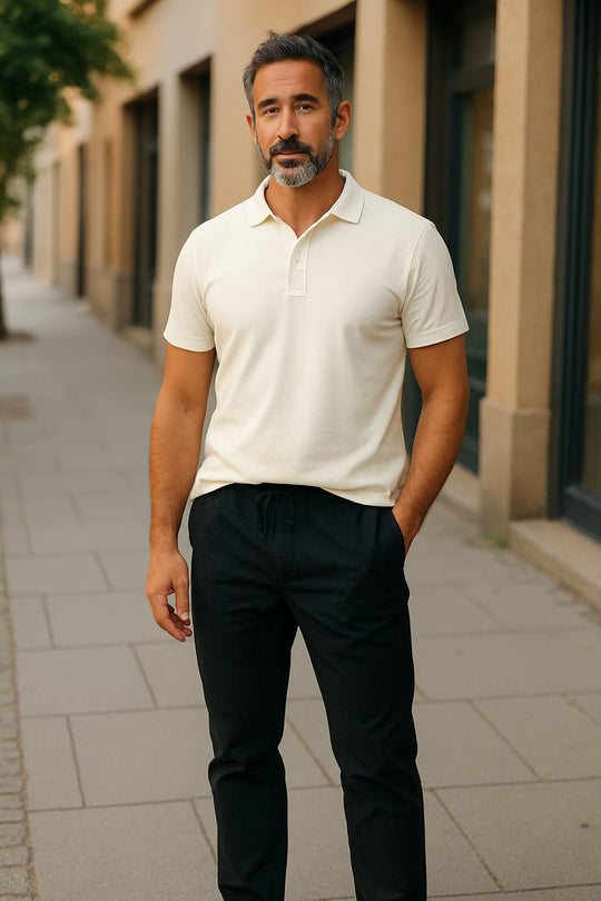 Man wearing a merino white polo shirt and black pants standing on a sidewalk.