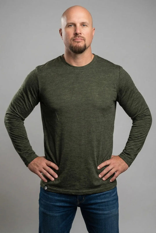 Man wearing a green long-sleeve shirt and blue jeans against a gray background