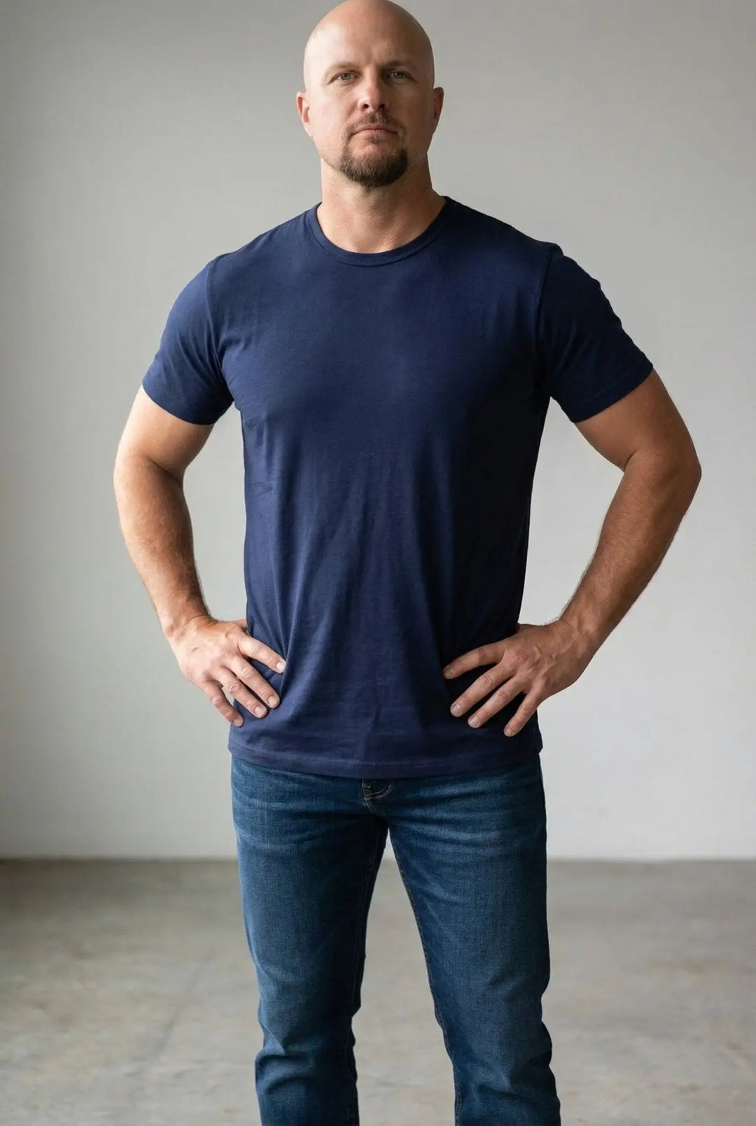 Man wearing a navy blue t-shirt and jeans against a plain background