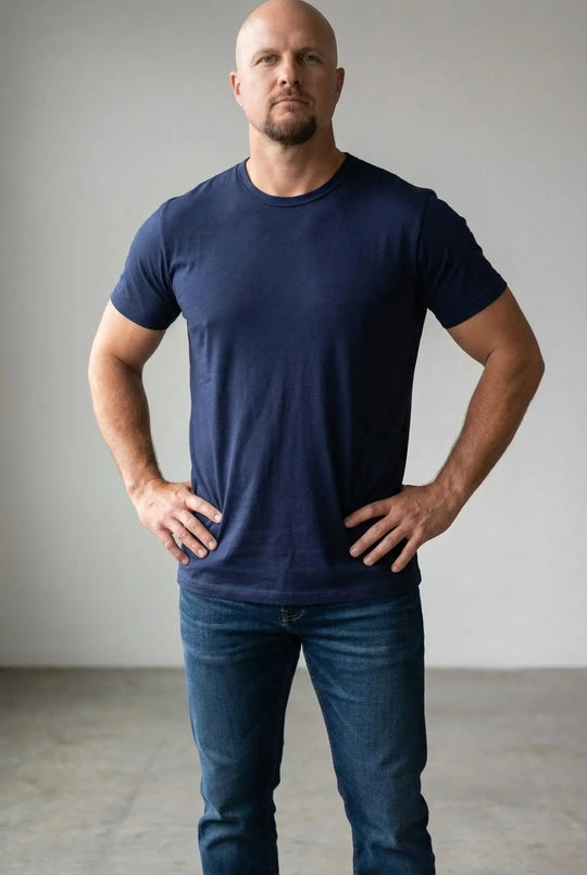 Man wearing a navy blue t-shirt and jeans against a plain background