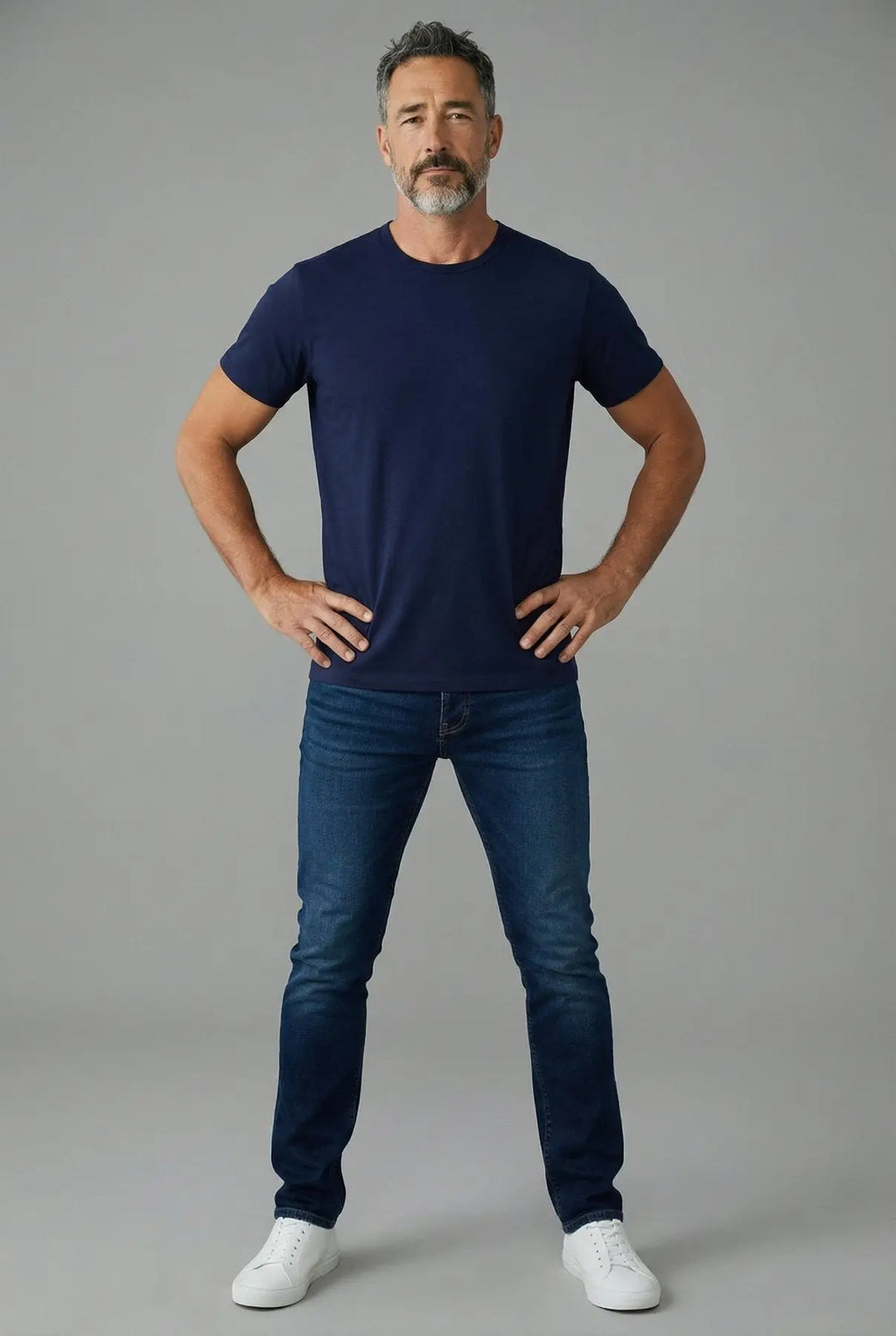 Man wearing a navy blue t-shirt and jeans on a gray background