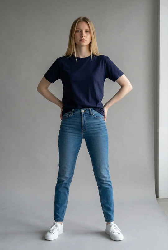 Person wearing a navy t-shirt and blue jeans standing against a plain background