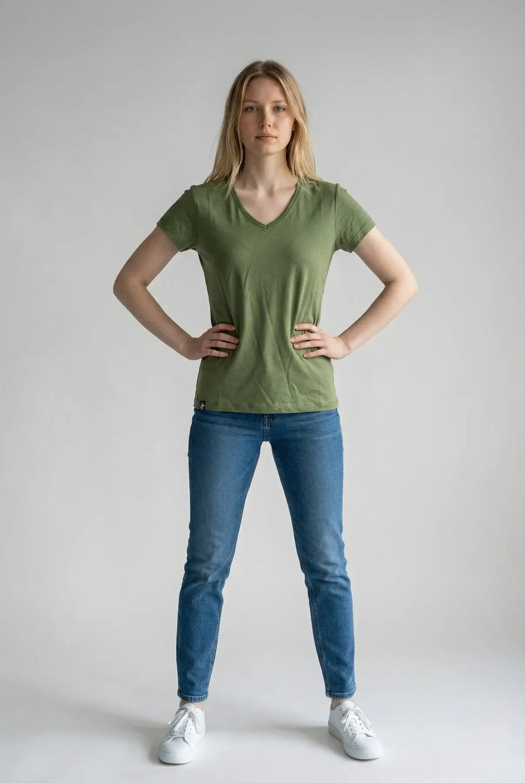 Woman wearing a green t-shirt and blue jeans on a plain background