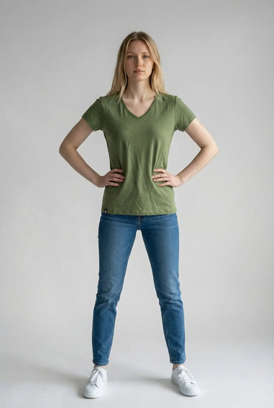 Woman wearing a green t-shirt and blue jeans on a plain background