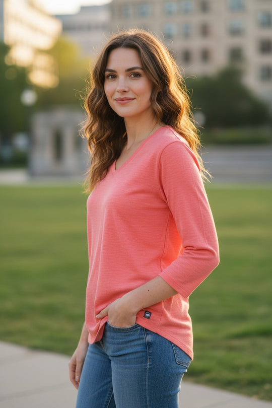 Woman wearing a pink long-sleeve top and blue jeans standing outdoors.