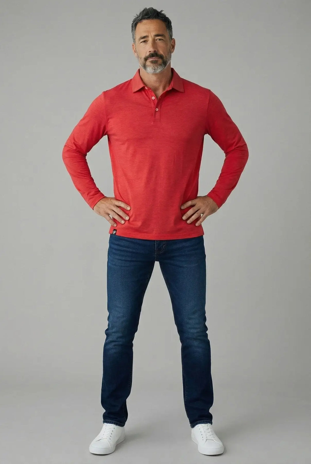 Man wearing a red long-sleeve polo shirt and blue jeans on a gray background