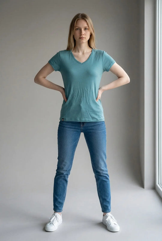 Woman wearing a teal t-shirt and blue jeans standing against a plain background