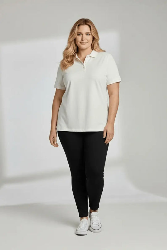 Woman wearing a white polo shirt and black leggings on a plain background