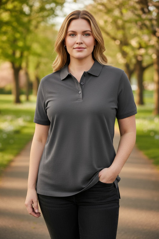 Woman wearing a gray polo shirt standing outdoors with trees in the background