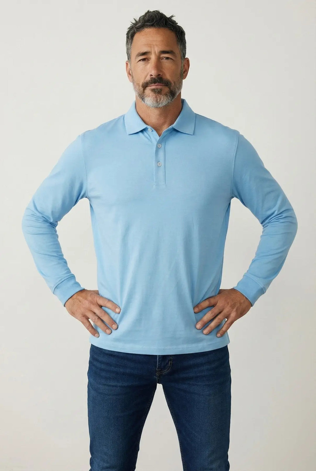 Man wearing a light blue long-sleeve polo shirt and dark jeans against a plain background
