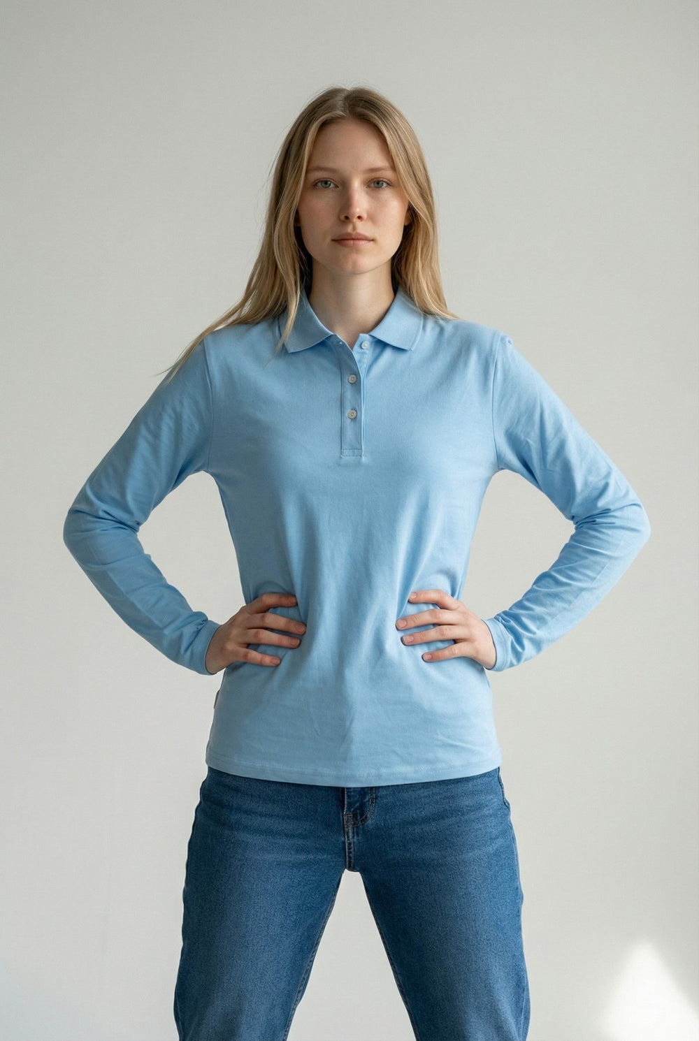 Woman wearing a light blue long-sleeve polo shirt and jeans against a plain background