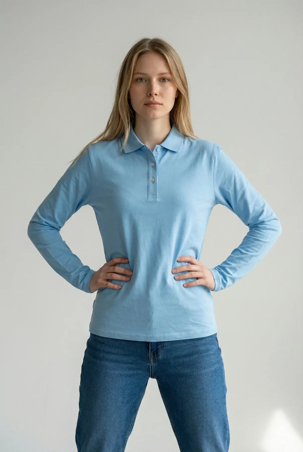 Woman wearing a light blue long-sleeve polo shirt and jeans against a plain background
