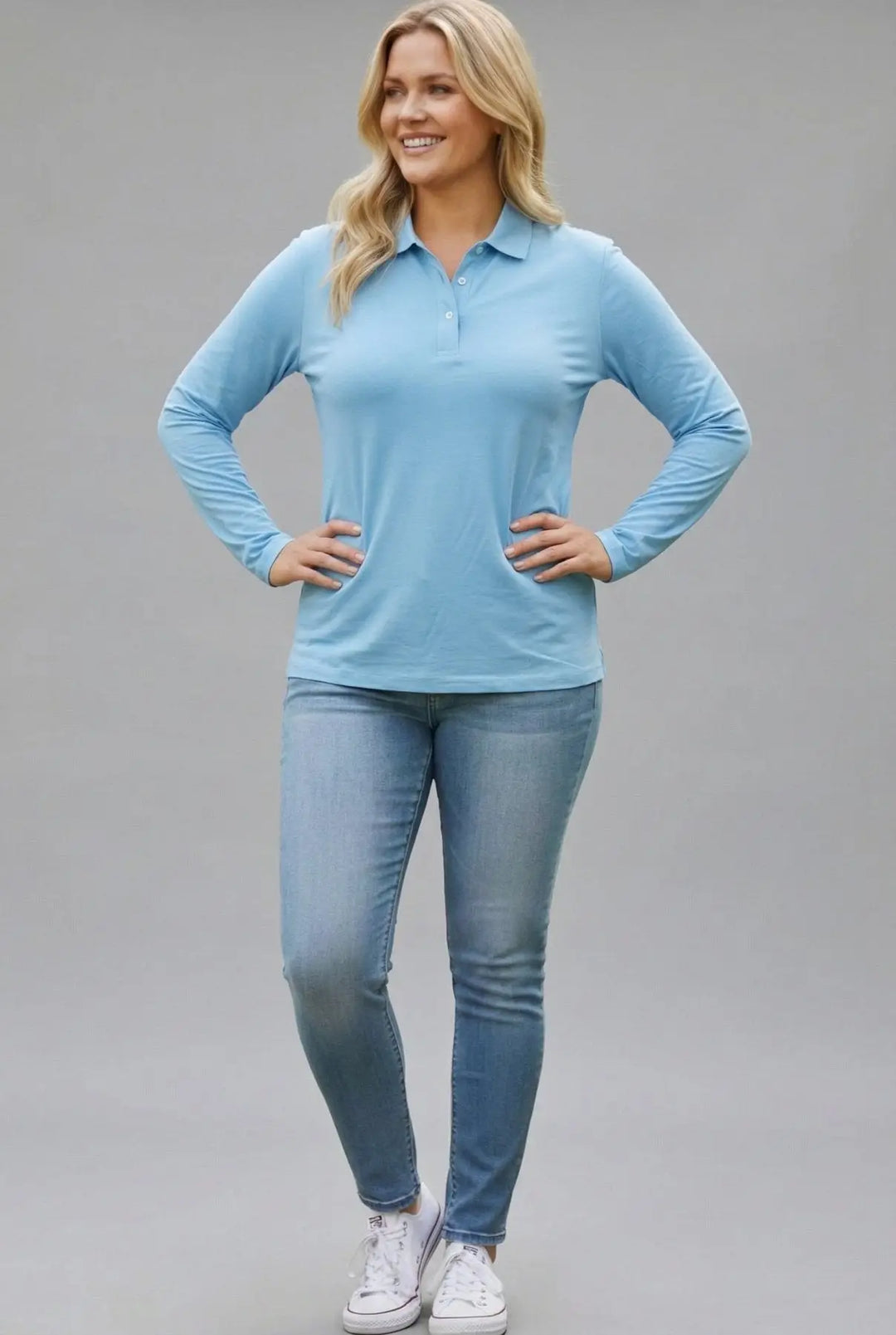 Woman wearing a light blue long-sleeve top and jeans on a gray background