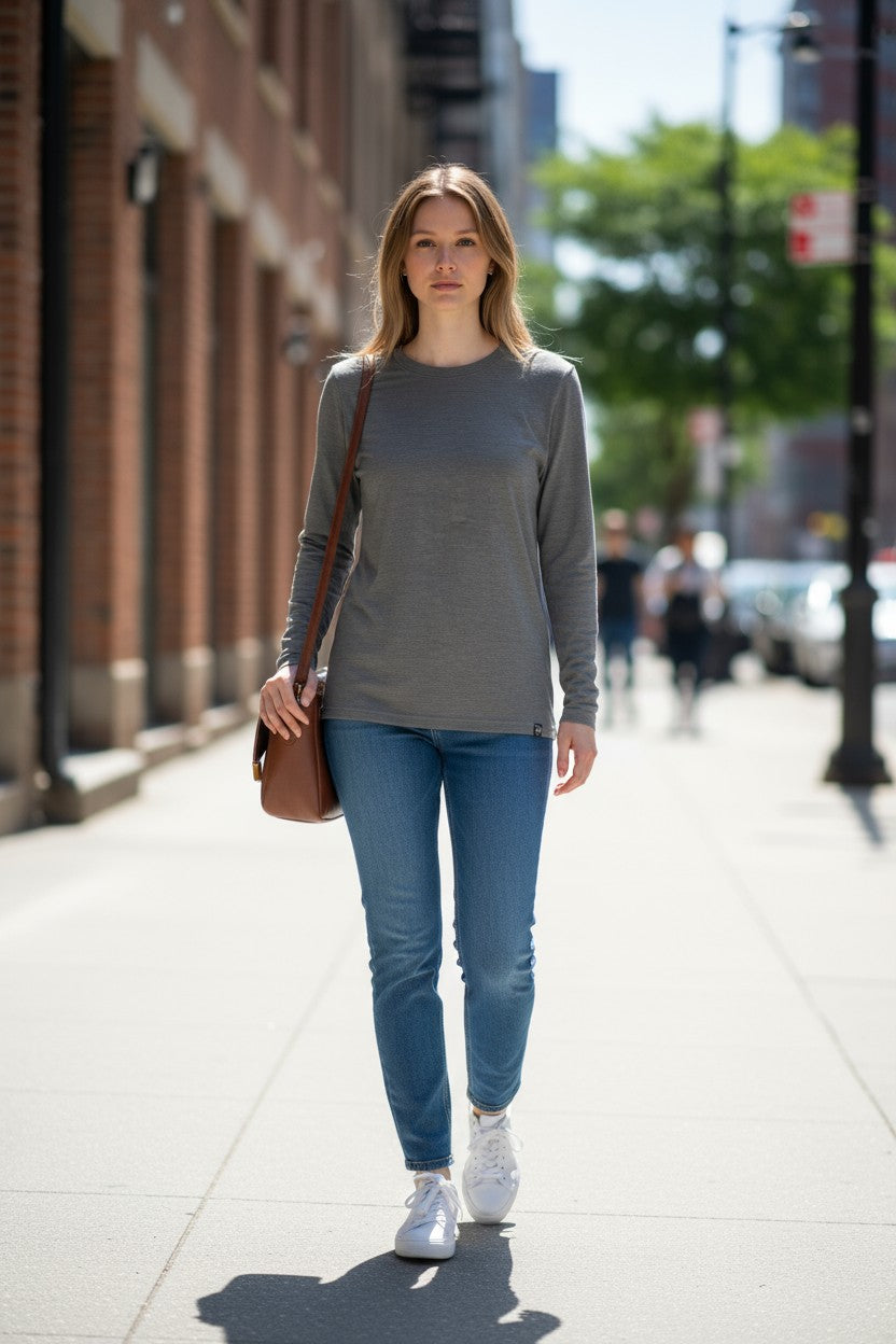 Woman walking on a city street wearing a gray long-sleeve top and blue jeans.