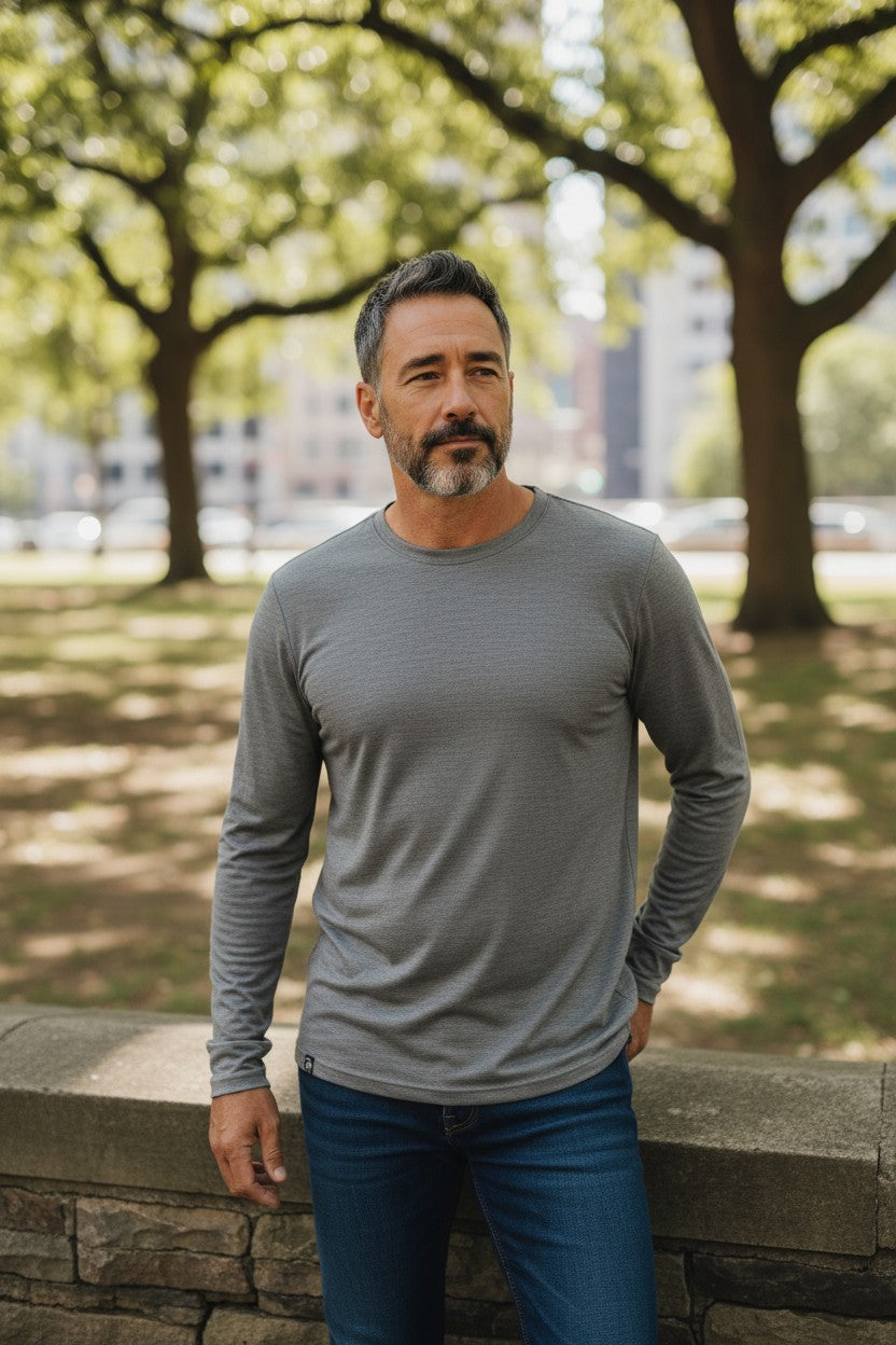 Man wearing a gray long-sleeve shirt and blue jeans standing outdoors with trees in the background