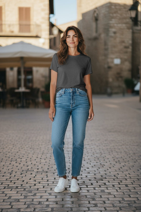 Woman standing on a cobblestone street wearing a gray t-shirt and blue jeans.
