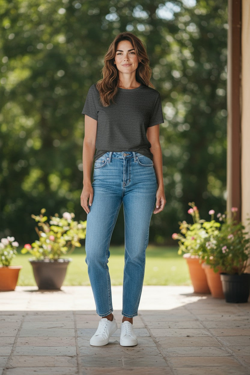 Woman wearing a black t-shirt and blue jeans standing outdoors with plants in the background