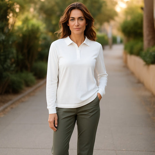 Woman wearing a white shirt and green pants standing on a sidewalk with trees in the background