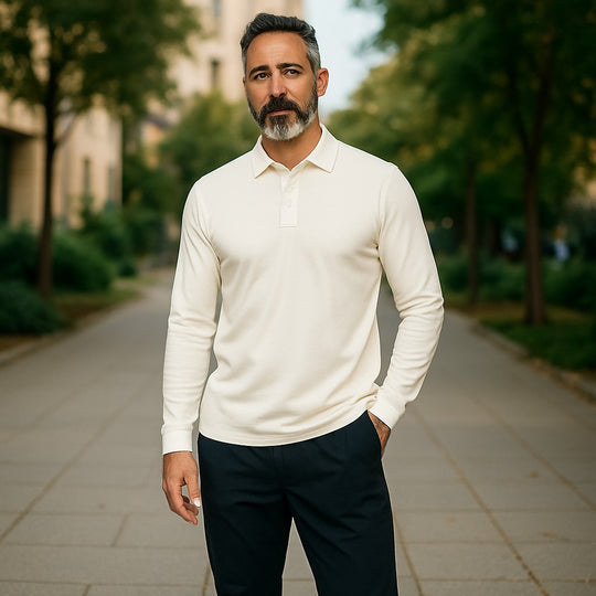 Man wearing a white long-sleeve shirt and dark pants standing outdoors on a path with greenery.