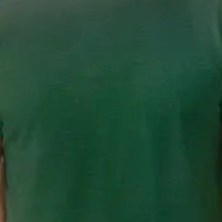 Man wearing a green t-shirt and blue jeans standing on a cobbled street with trees and buildings in the background.