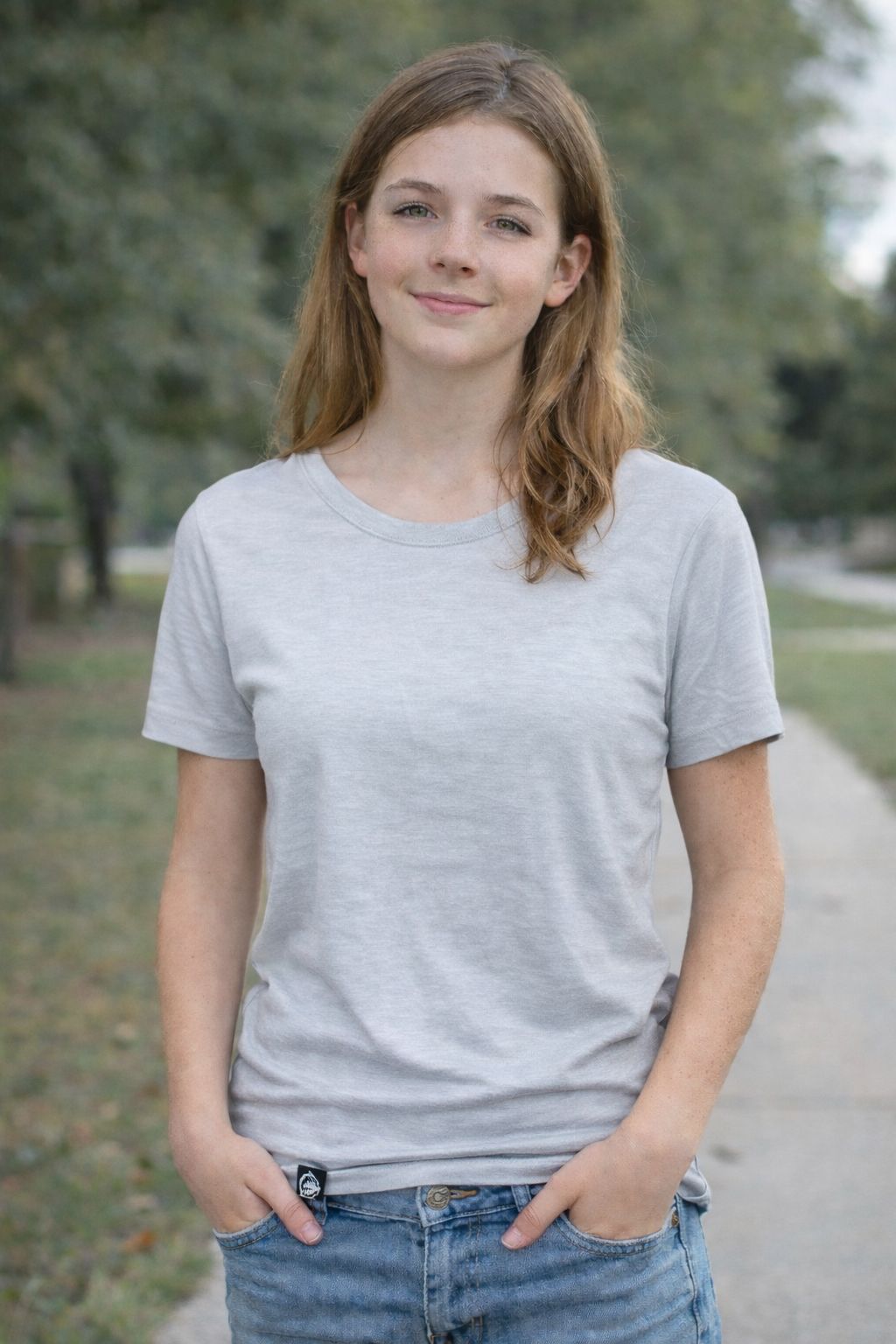 Person wearing a glacier blue t-shirt and blue jeans standing outdoors with trees in the background