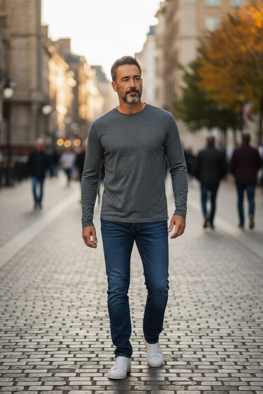 Man walking on a city street wearing a gray long-sleeve shirt and blue jeans.