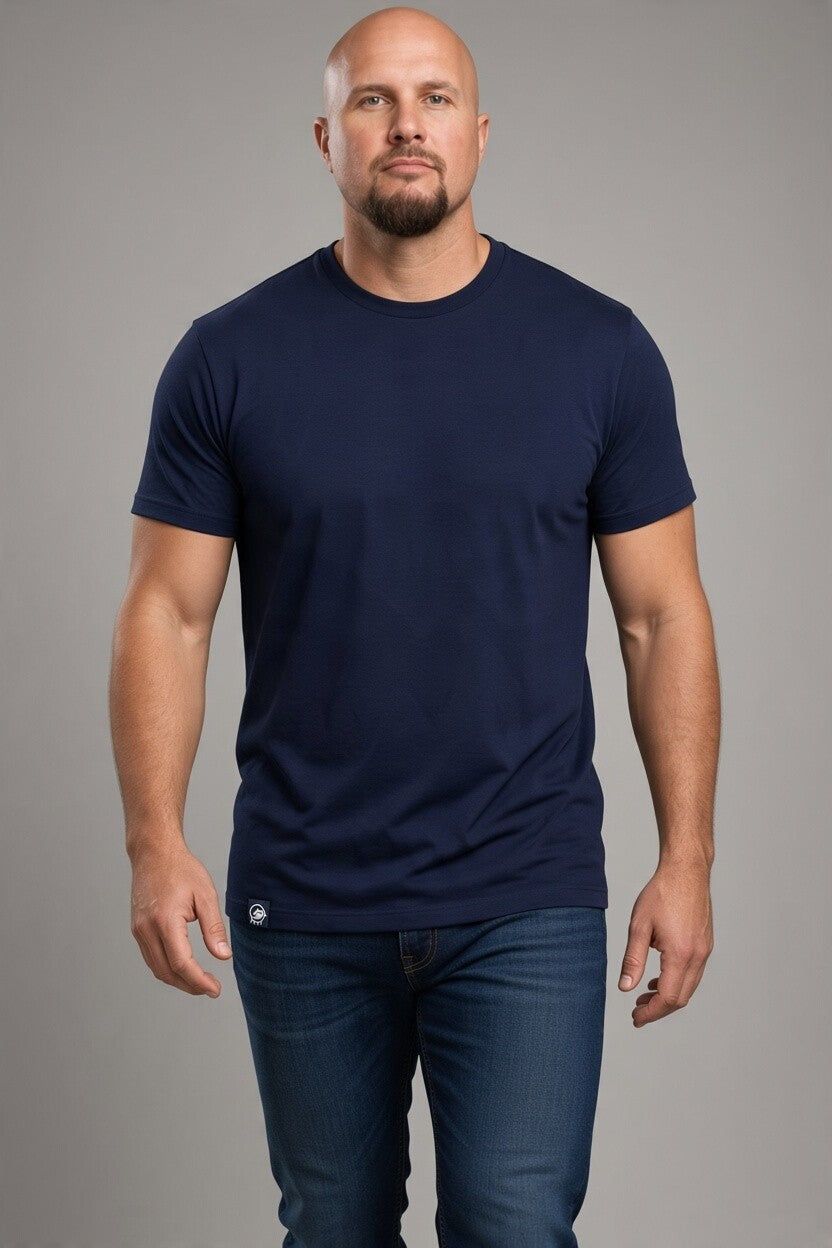 A bald man with a beard modeling a dark navy blue crew-neck t-shirt and dark blue jeans against a solid gray studio background.