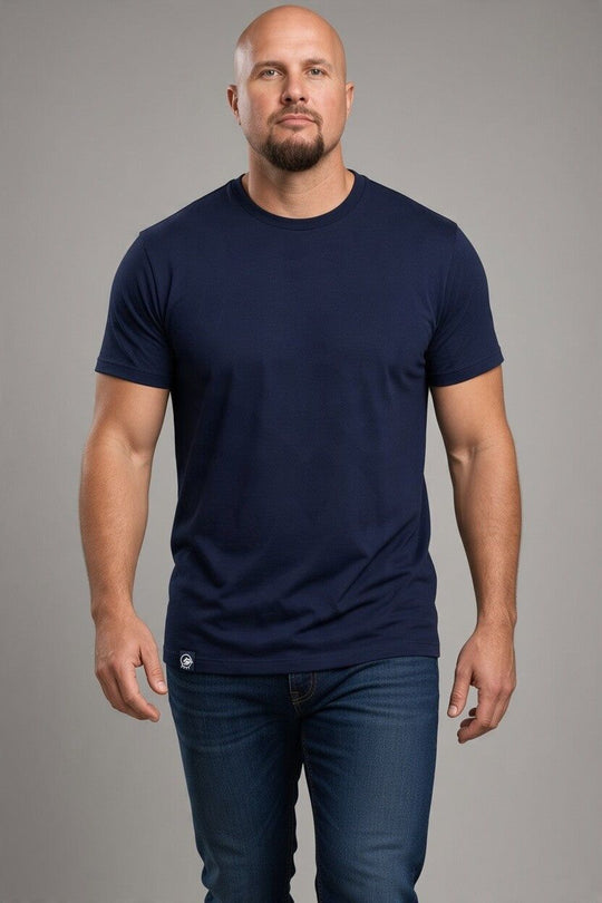 A bald man with a beard modeling a dark navy blue crew-neck t-shirt and dark blue jeans against a solid gray studio background.