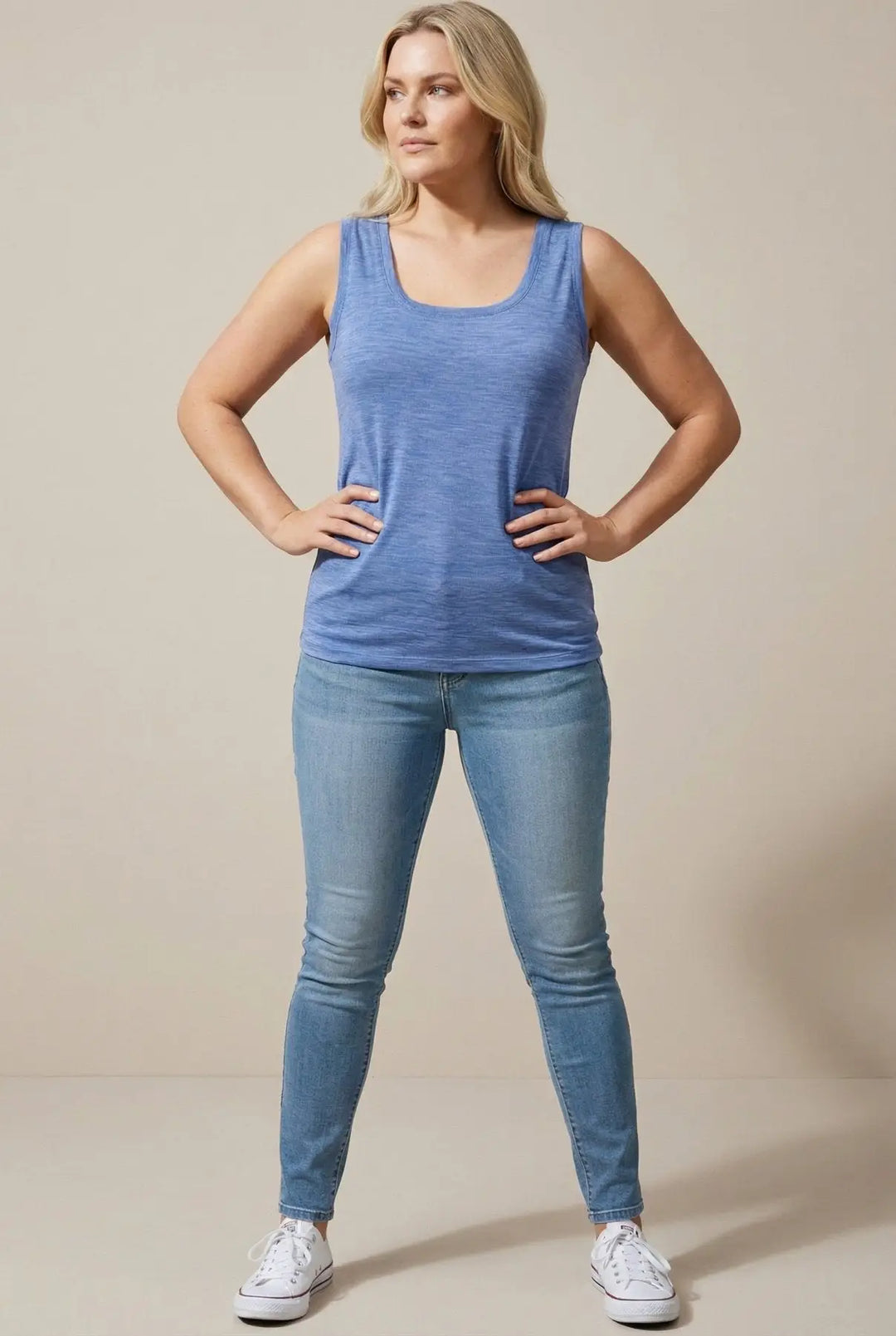 Woman wearing a blue tank top and jeans against a beige background