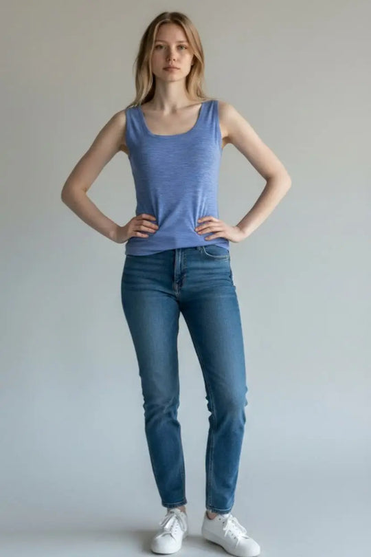 Woman wearing a blue tank top and jeans against a plain background