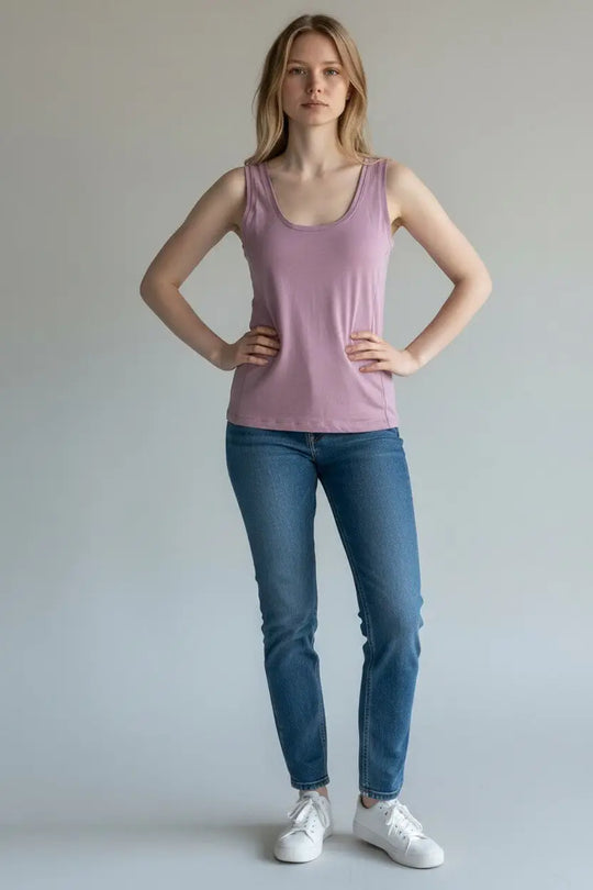 Woman wearing a pink tank top and blue jeans against a plain background