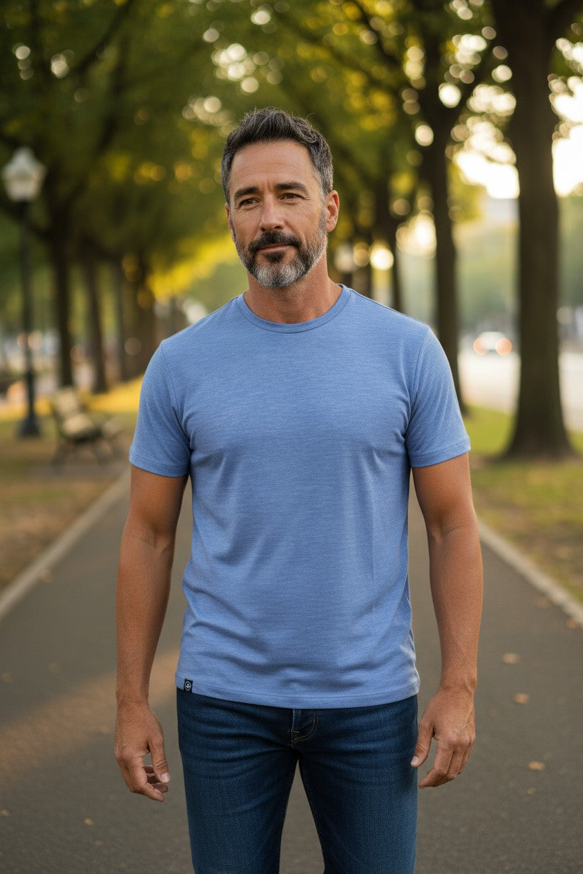 Man wearing a blue t-shirt standing on a tree-lined street.