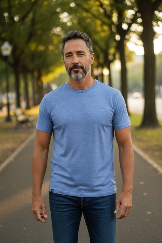 Man wearing a blue t-shirt standing on a tree-lined street.