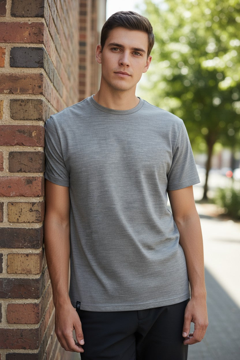 Man wearing a gray t-shirt leaning against a brick wall outdoors.