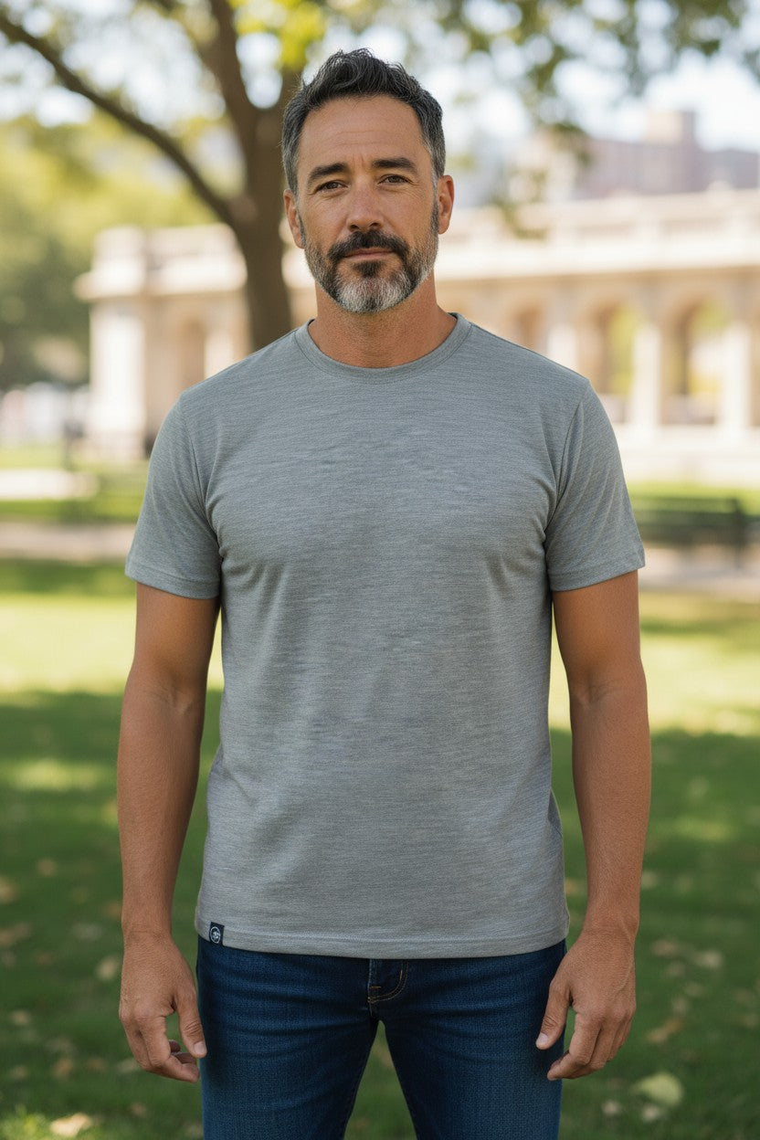 Man wearing a gray t-shirt standing outdoors with greenery in the background