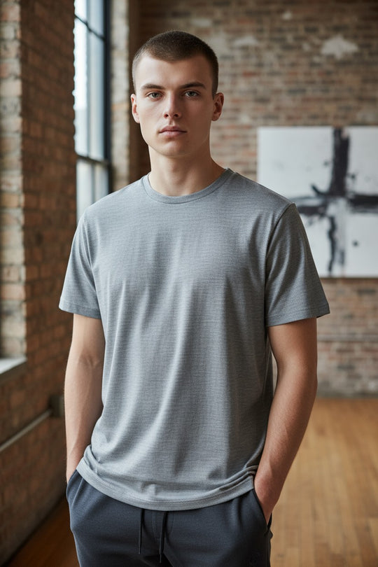 Man wearing a gray t-shirt standing in a room with brick walls and a painting.